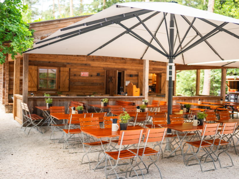 Der Biergarten des Waldgartens der Fater Alm im Münchner Wald. Gemütliche Biertische, Sonnenschirme und mehr.