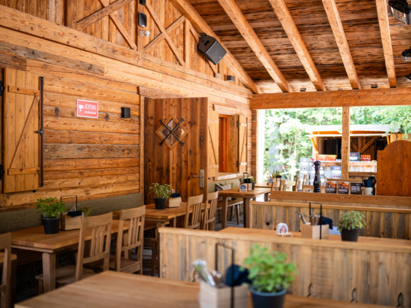 Die Terrasse vor der Fater Alm, welche unter dem Dach ist. Mit Holztischen und - stühlen. Schon gedeckt und geschmückt.