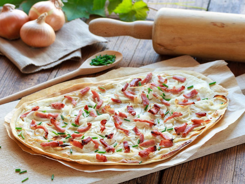 Ein Flammkuchen mit Speck und Zwiebeln, auf einem Holzbrett. Dekoriert mit Schnittlauch.