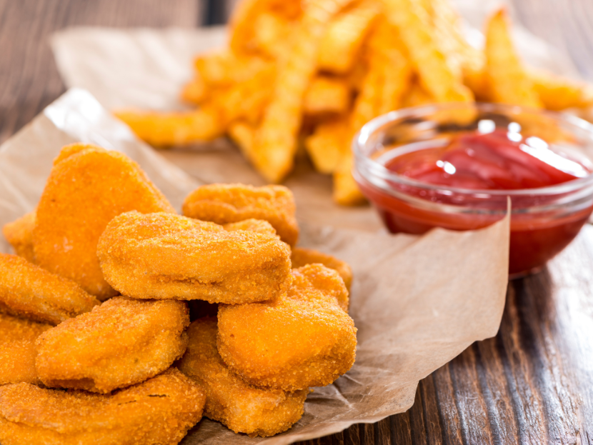Knusprige Nuggets sowie golden gebratene Pommes. Daneben ein kleines Glas gefüllt mit Tomaten-Ketchup.